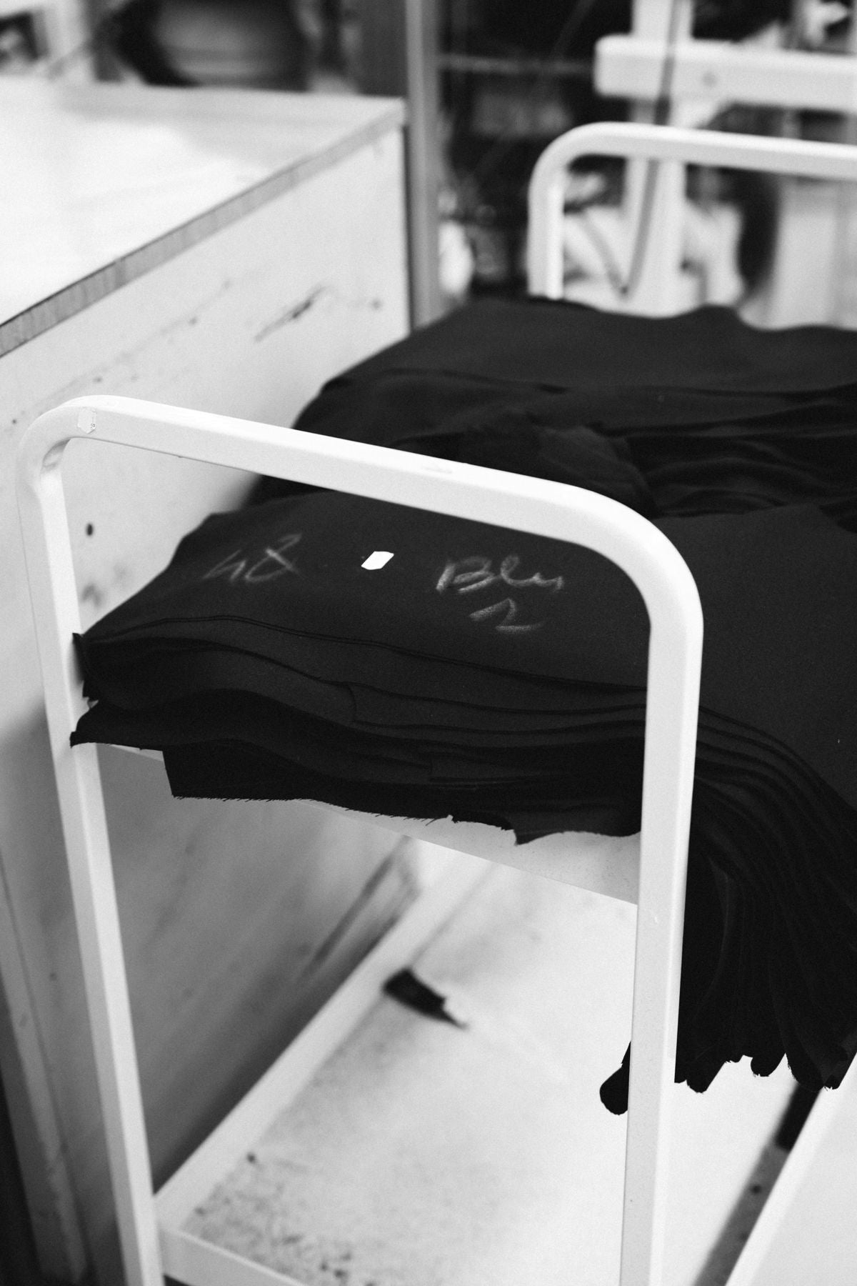 A stack of cut wool pieces chalk-marked Blu on a factory cart, in black and white
