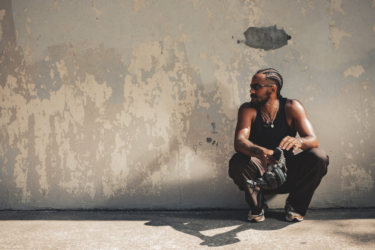 Liam in Once in a Blue pleated trousers crouching in the sun in front of a weathered wall in New York