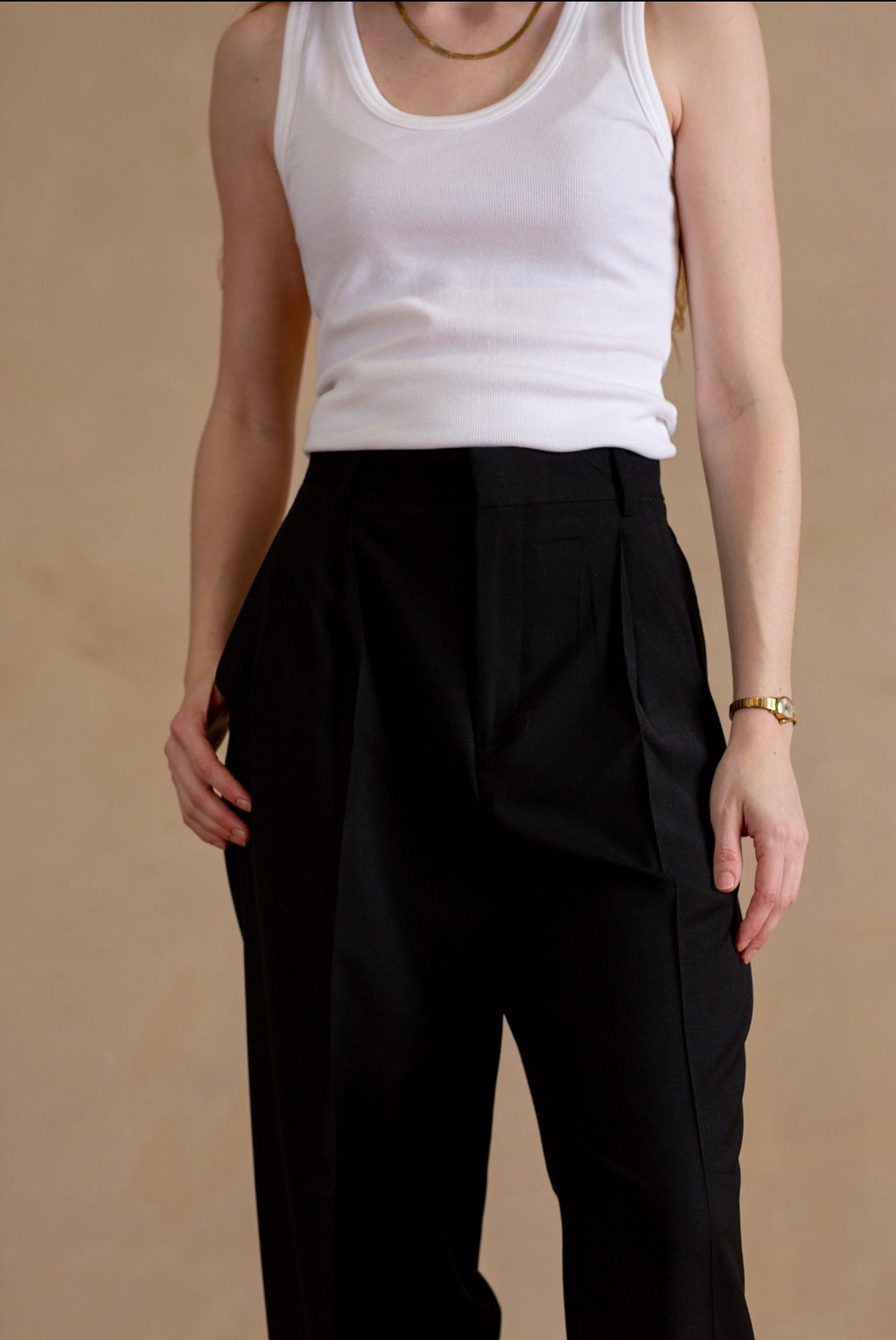 Person wearing a white tank top and black pants on a beige background