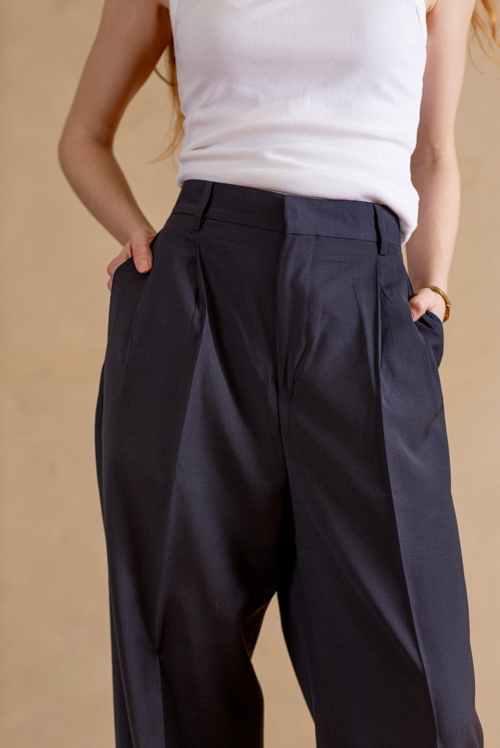 Person wearing navy pants and a white top on a beige background