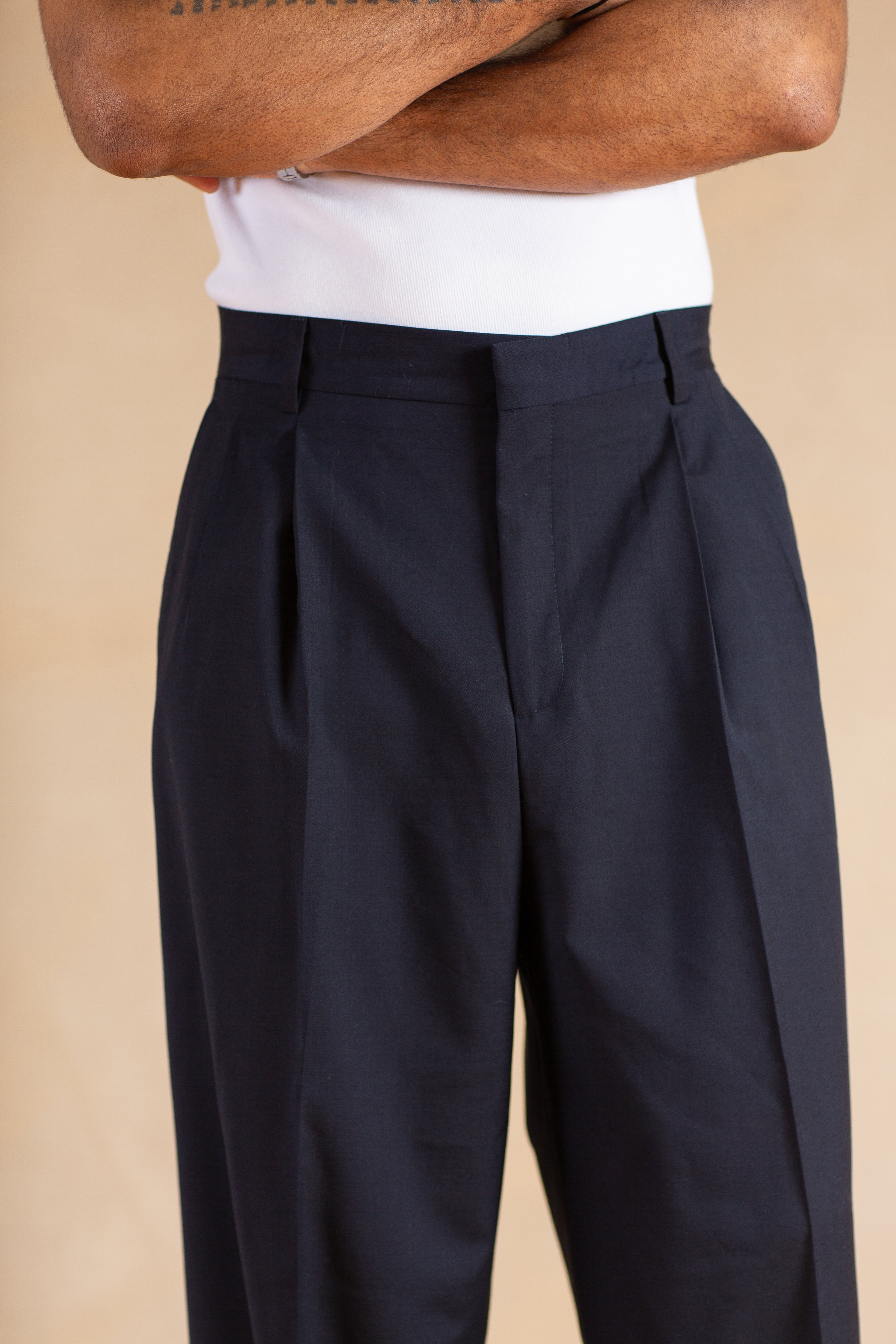 Person wearing navy pleated pants on a beige background