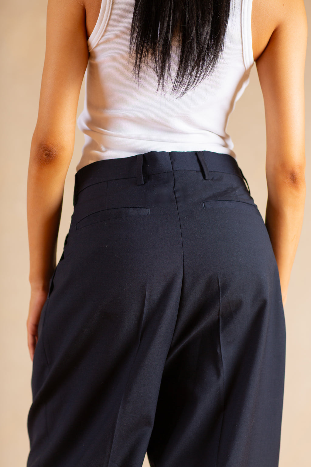 Person wearing Navy pants and a white top against a beige background