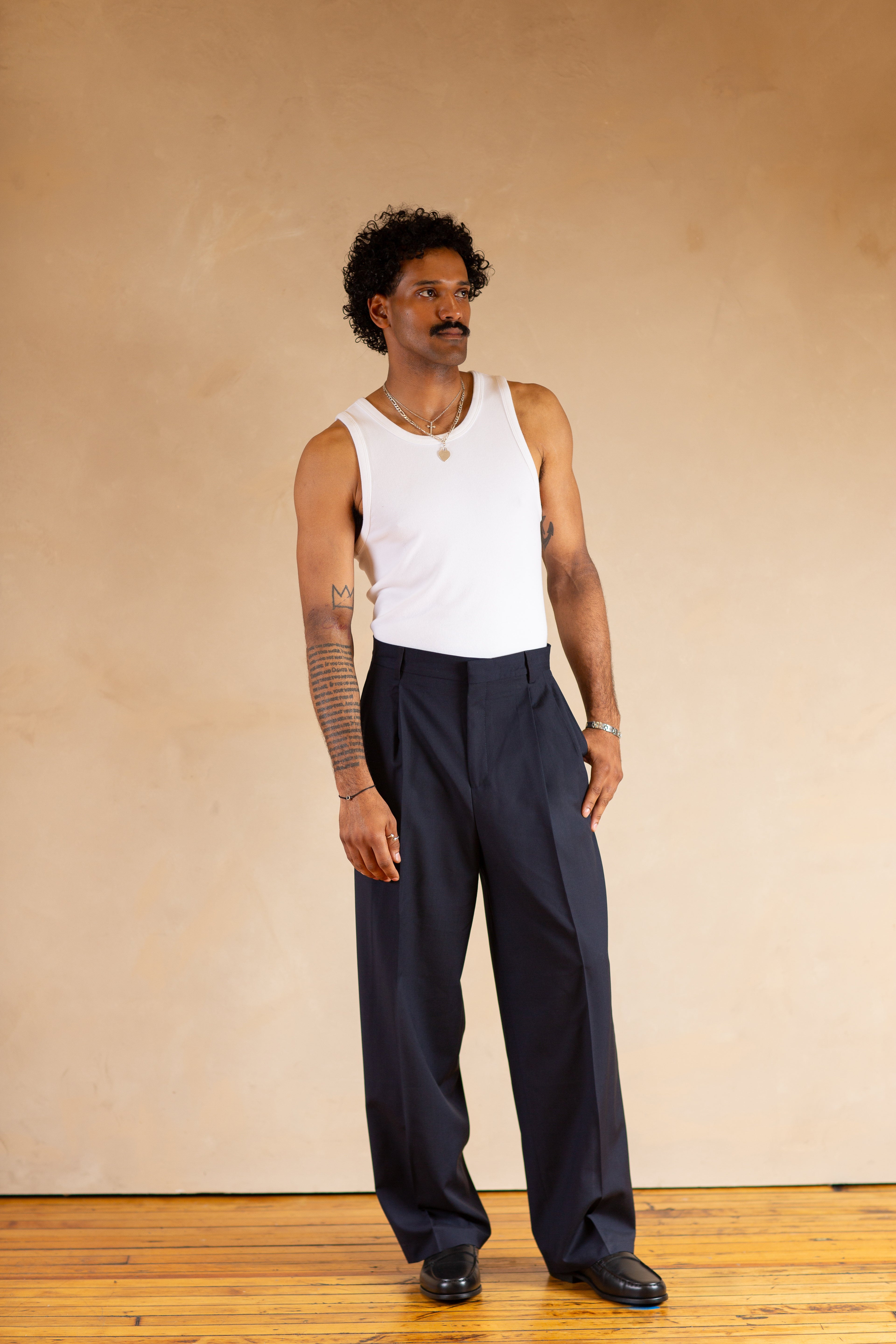 Person wearing a white tank top and Navy pants against a beige background