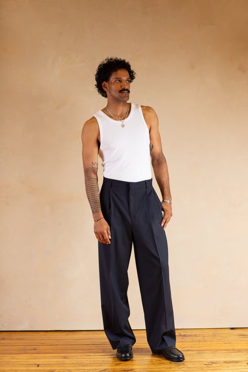 Person wearing a white tank top and Navy pants against a beige background