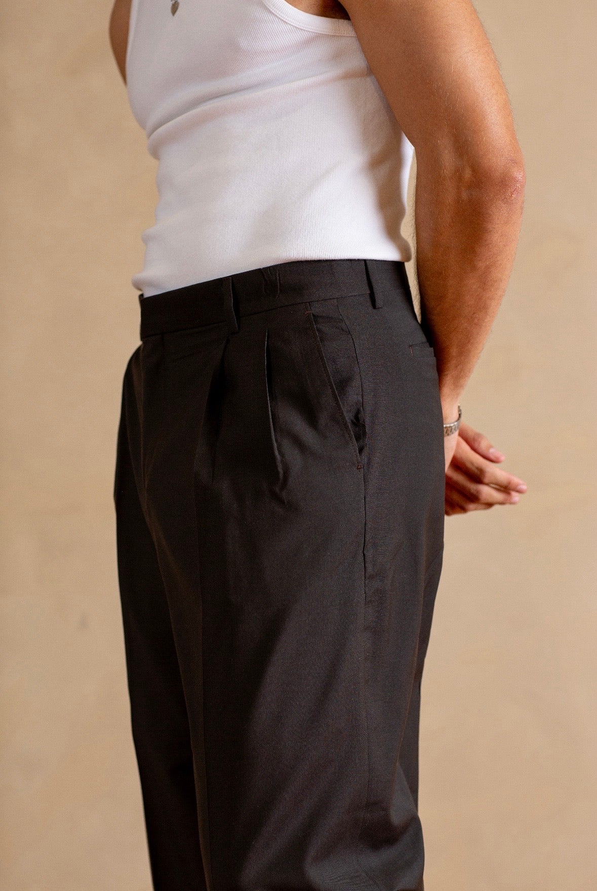 Person wearing a white tank top and Stone pants on a beige background