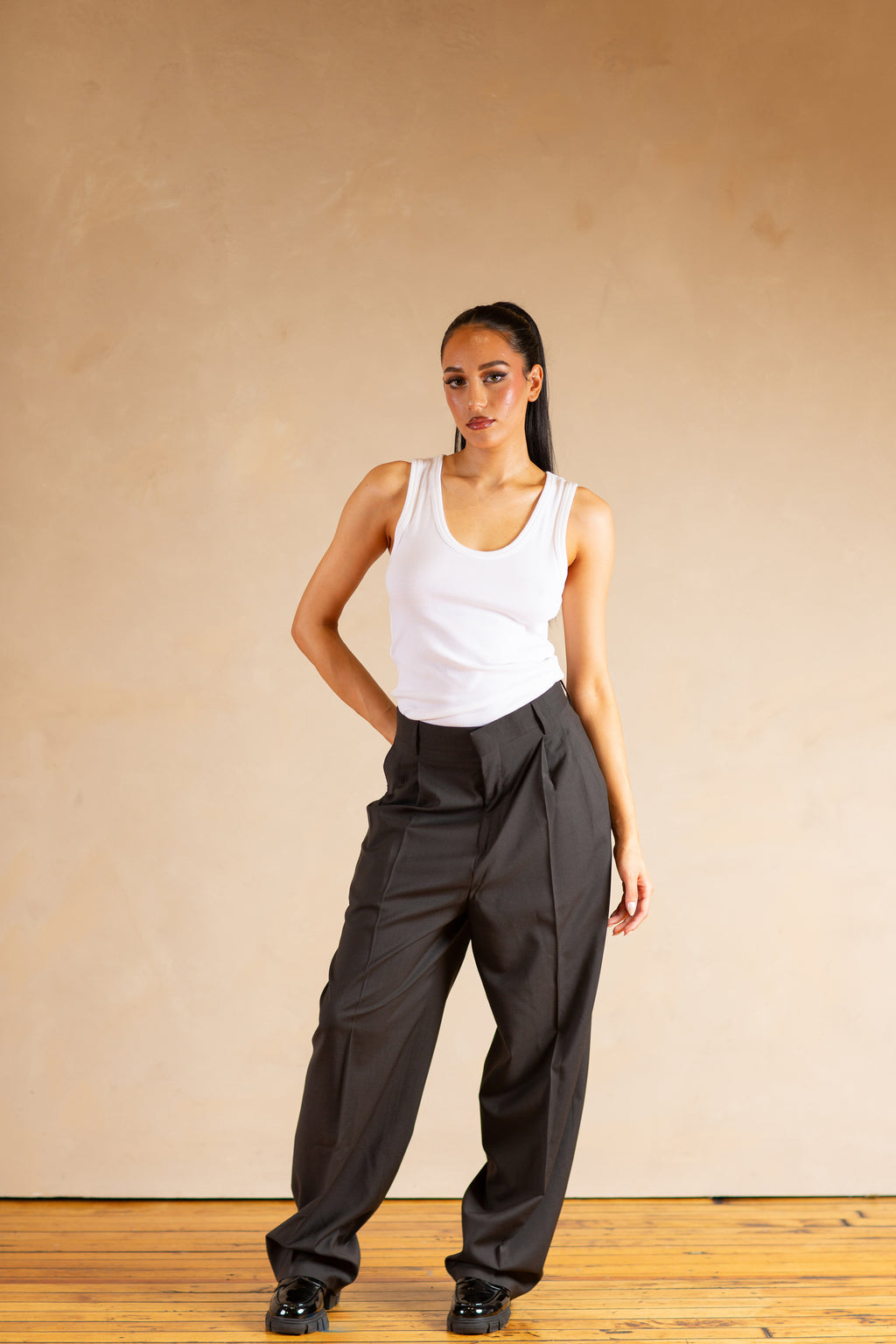 Woman wearing a white tank top and Stone pants against a beige background
